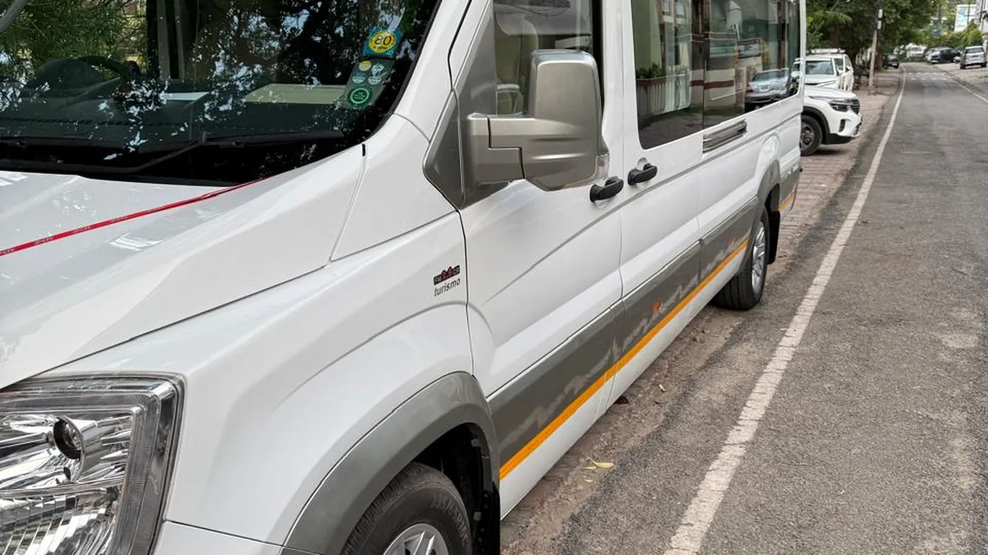 A white Force Urbania parked kerbside on a tree-lined Varanasi road, seen along its full length